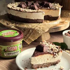 Pyszne ciasto Kinder Bueno z mascarpone, udekorowane orzechami i czekoladkami. Obok słoik pasty z orzechów laskowych.
