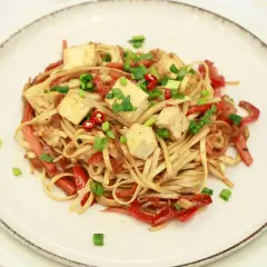 Pyszny makaron z tofu, papryką i szczypiorkiem, posypany chili. Danie wygląda apetycznie i kolorowo.