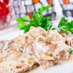 Schab w sosie koperkowym, podany na białym talerzu, udekorowany świeżą natką pietruszki.