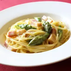 Pyszna carbonara ze szparagami, podana w białej misce na czerwonym tle.