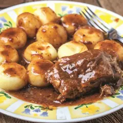 Mięciutka karkówka w sosie, podana z kluskami śląskimi na talerzu z żółto-białym wzorem.