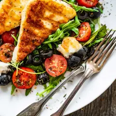 Pyszna sałatka z grillowanym halloumi, pomidorkami koktajlowymi i czarnymi oliwkami na talerzu, gotowa do zjedzenia.