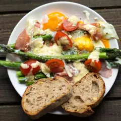 Pyszne szparagi z szynką parmeńską, jajkiem sadzonym i pomidorkami, polane sosem. Podane z chlebem.