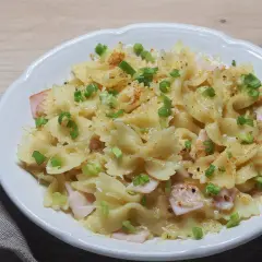 Pyszne dania z makaronem w kształcie motylków, z kawałkami szynki, posypane szczypiorkiem i przyprawami.