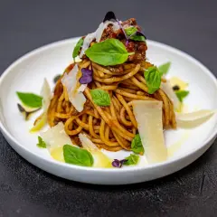 Pyszne spaghetti alla norma z sosem pomidorowym, bakłażanem i parmezanem, ozdobione listkami bazylii.