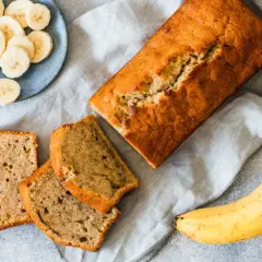Chlebek bananowy pokrojony na kromki, obok banany i talerzyk z plasterkami banana.