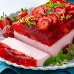 Pyszne ciasto bez pieczenia z truskawkami i galaretką, udekorowane miętą i pistacjami. Idealne na letnie popołudnie.