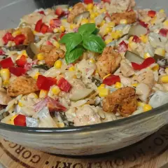 Pyszna sałatka z kurczakiem, makaronem orzo, kukurydzą, papryką i ogórkiem kiszonym, udekorowana listkiem bazylii.
