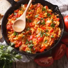 Pyszna jajecznica z pomidorami i natką pietruszki, podana w żeliwnej patelni, obok kromek chleba i świeżych pomidorów.