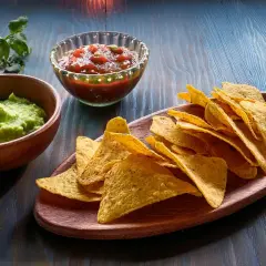 Chrupiące chipsy z tortilli, guacamole i salsa na drewnianej desce. Idealna przekąska na imprezę.