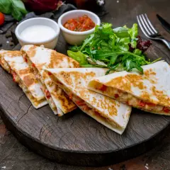 Pyszna quesadilla z kurczakiem, podana z salsą, śmietaną i sałatką na drewnianej desce.