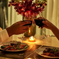 Romantyczna kolacja dla dwojga przy świecach. Dwie pary kieliszków z czerwonym winem unoszą się w powietrzu, a na talerzach czekają pyszne dania.