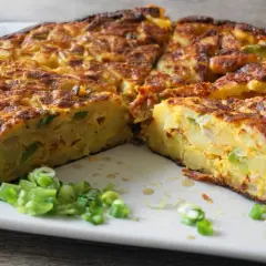 Pyszna tortilla de patatas, pokrojona na kawałki, z zieloną cebulką na talerzu.