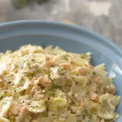 Pyszny makaron farfalle z kawałkami łososia w kremowym sosie, posypany świeżym koperkiem i pieprzem.