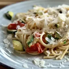 Pyszny makaron z pomidorkami koktajlowymi i cukinią, posypany parmezanem. Idealny letni posiłek.