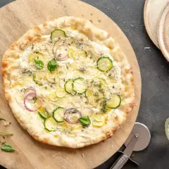 Pyszny spód do pizzy z cukinią, cebulą i ziołami, podany na drewnianej desce.