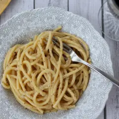 Porcja pysznego cacio e pepe na ozdobnym talerzu, z widelcem w makaronie.