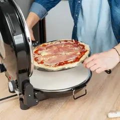 Osoba wkłada pizzę z szynką do pieca. Szybko i łatwo przygotujesz idealną pizzę w domu.