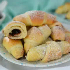 Stos puszystych rogalików z marmoladą, posypanych cukrem pudrem, czeka na spróbowanie.