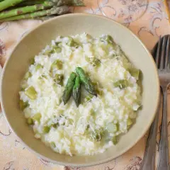 Kremowe risotto ze szparagami, posypane parmezanem, z trzema młodymi pędami szparagów na wierzchu.