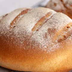 Chleb na maślance, lekko oprószony mąką, z widocznymi nacięciami na skórce. Pachnie świeżością i domowym ciepłem.