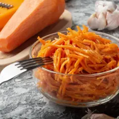 Pyszna surówka z marchewki, gotowa do podania. Obok świeża marchewka, tarka, czosnek i papryczka chili.