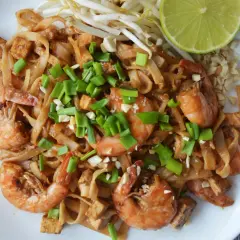 Pyszne pad thai z krewetkami, makaronem ryżowym, tofu i szczypiorkiem, podane z limonką i orzeszkami ziemnymi.