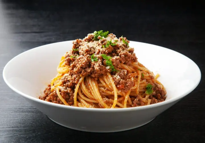 Pyszne spaghetti z bogatym sosem bolognese, posypane parmezanem i natką pietruszki. Idealne danie z makaronem z mięsem mielonym.