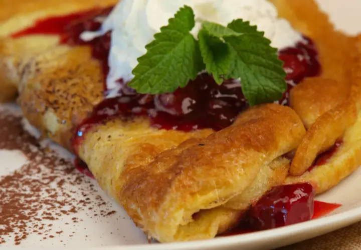 Pyszny omlet Ani gotuje się z wiśniami i bitą śmietaną, posypany kakao.
