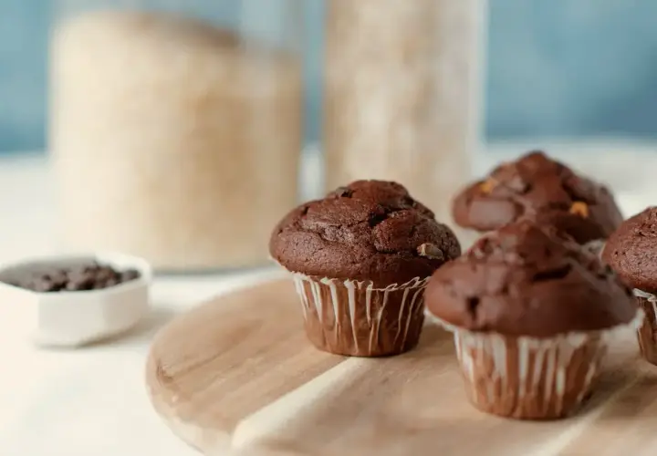 Pyszne muffinki z czekoladą, gotowe do zjedzenia. W tle słoiki z cukrem i mąką.
