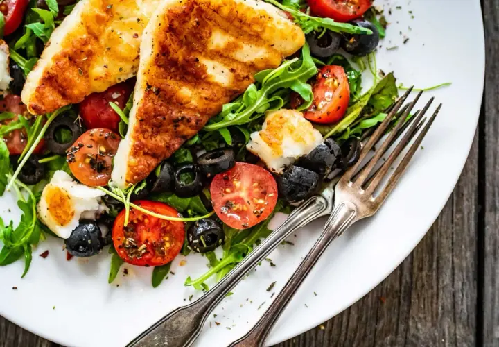 Pyszna sałatka z grillowanym halloumi, pomidorkami koktajlowymi i czarnymi oliwkami na talerzu, gotowa do zjedzenia.