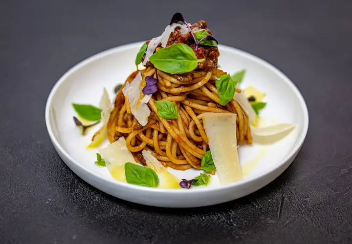 Pyszne spaghetti alla norma z sosem pomidorowym, bakłażanem i parmezanem, ozdobione listkami bazylii.