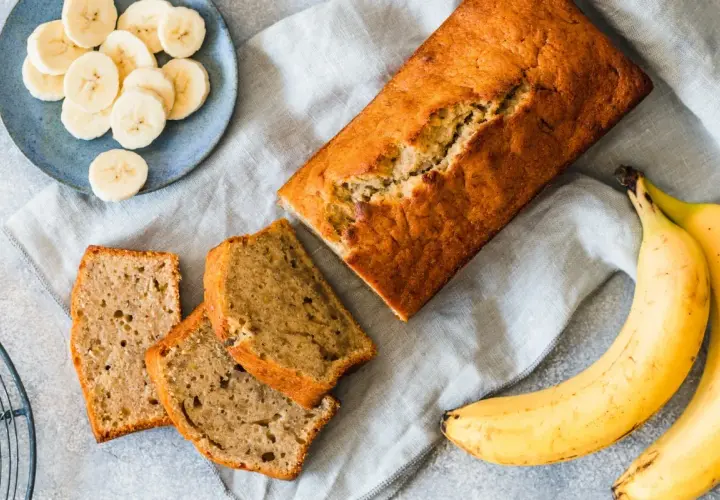 Chlebek bananowy pokrojony na kromki, obok banany i talerzyk z plasterkami banana.