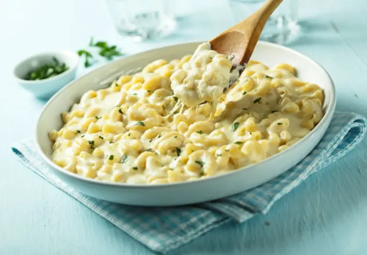 Pyszne mac and cheese przepis w białej misce, z drewnianą łyżką nabierającą porcję kremowego makaronu z serem.