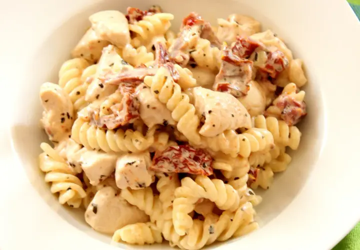 Pyszny makaron fusilli z kawałkami kurczaka i aromatycznymi suszonymi pomidorami w kremowym sosie.