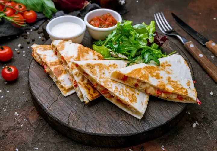Pyszna quesadilla z kurczakiem, podana z salsą, śmietaną i sałatką na drewnianej desce.