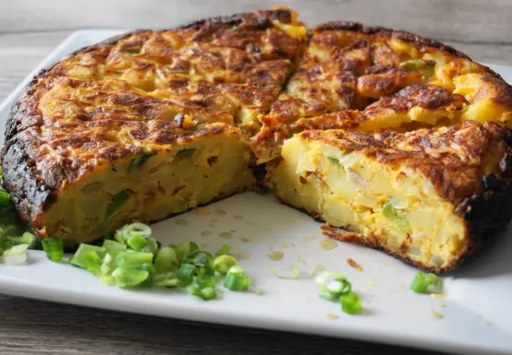 Pyszna tortilla de patatas, pokrojona na kawałki, z zieloną cebulką na talerzu.