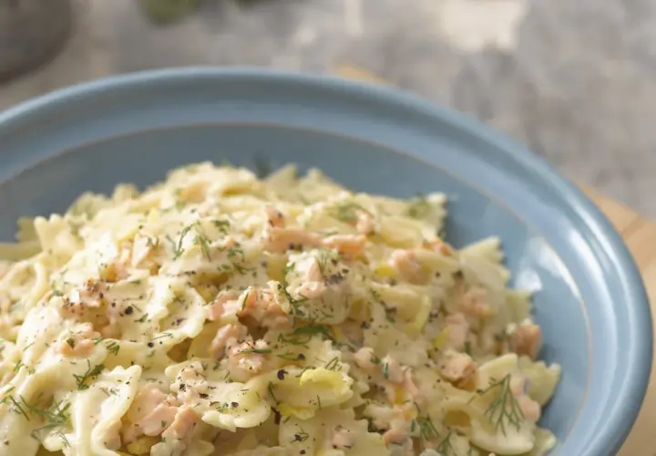 Pyszny makaron farfalle z kawałkami łososia w kremowym sosie, posypany świeżym koperkiem i pieprzem.