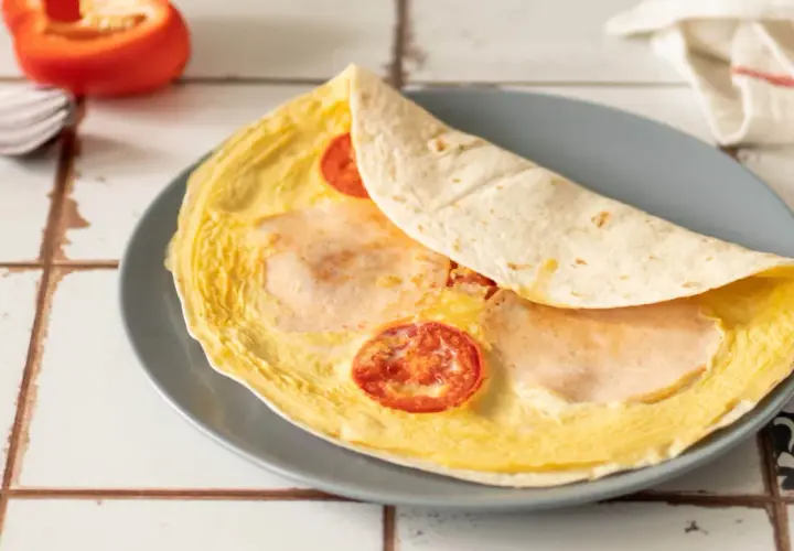 Pyszna, ciepła kolacja: omlet z tortillą, pomidorkami i szynką. Idealny na szybki posiłek.