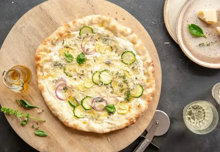 Pyszny spód do pizzy z cukinią, cebulą i ziołami, podany na drewnianej desce.