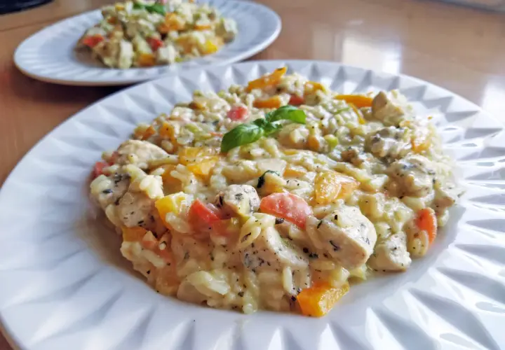 Pyszne risotto z kurczakiem, papryką i bazylią, podane na białym talerzu. Idealne na obiad.
