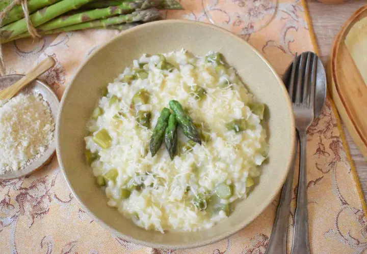 Kremowe risotto ze szparagami, posypane parmezanem, z trzema młodymi pędami szparagów na wierzchu.