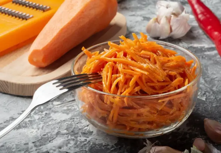 Pyszna surówka z marchewki, gotowa do podania. Obok świeża marchewka, tarka, czosnek i papryczka chili.