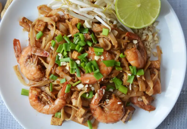 Pyszne pad thai z krewetkami, makaronem ryżowym, tofu i szczypiorkiem, podane z limonką i orzeszkami ziemnymi.