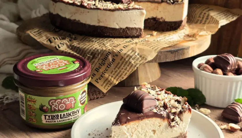 Pyszne ciasto Kinder Bueno z mascarpone, udekorowane orzechami i czekoladkami. Obok słoik pasty z orzechów laskowych.