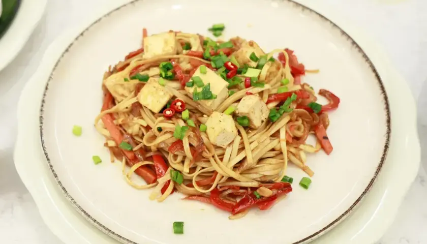 Pyszny makaron z tofu, papryką i szczypiorkiem, posypany chili. Danie wygląda apetycznie i kolorowo.