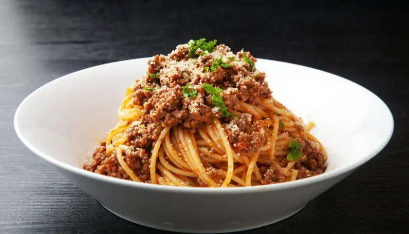 Pyszne spaghetti z bogatym sosem bolognese, posypane parmezanem i natką pietruszki. Idealne danie z makaronem z mięsem mielonym.