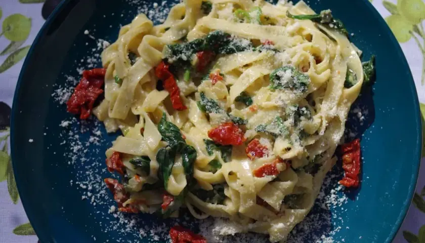 Pyszny makaron ze szpinakiem i suszonymi pomidorami, posypany parmezanem. Idealny na szybki obiad.