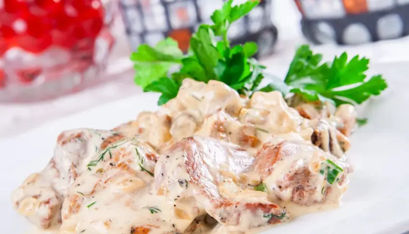 Schab w sosie koperkowym, podany na białym talerzu, udekorowany świeżą natką pietruszki.