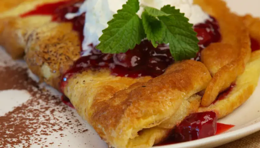 Pyszny omlet Ani gotuje się z wiśniami i bitą śmietaną, posypany kakao.
